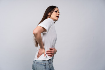 Brunette in white t-shirt on a gray background, the girl holding his hands behind his back, concept...