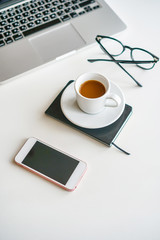 on a table on a white background is a coffee mug, laptop, glasses and a phone
