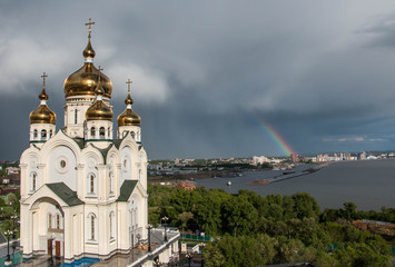 Сloud and rainbow over the city. Temple with golden domes