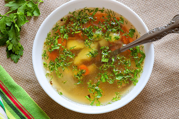 vegetable soup, homemade lunch background, broth with vegetables and herbs in a white plate