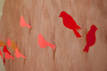 Several handmade red paper birds in line hanging on bast string on wall brouwn bacground. Red paper bird on the clothesline. Summer wedding theme. Love and valentine in nature.