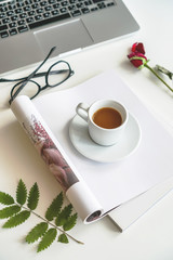 a mug of coffee stands on a magazine, beside it are glasses and a red rose. Worth a laptop