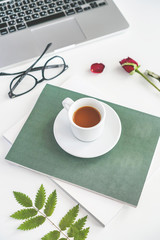 a mug of coffee stands on a magazine, beside it are glasses and a red rose. Worth a laptop