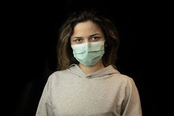 Studio portrait of young woman wearing a face mask, looking at camera, close up, isolated on black background