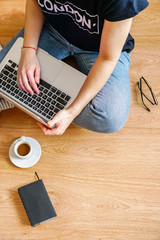 a girl sits on the floor with a laptop, near are glasses and a notebook for notes