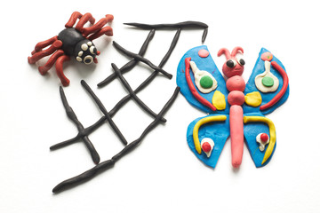 Spider caught a butterfly in its web. The scene is molded of multi-colored plasticine on white background