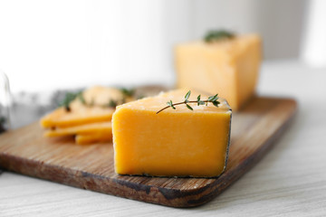 Wooden board with tasty cheese and thyme on white table