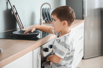 Little boy playing with frying pan on electric stove at home