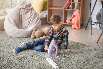 Little boy playing with electric iron at home