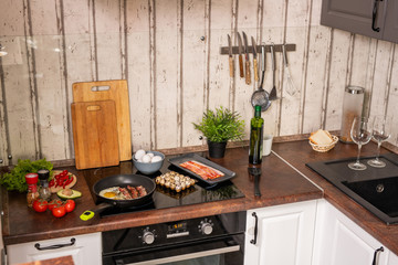 Part of contemporary kitchen with electric stove with frying bacon and eggs