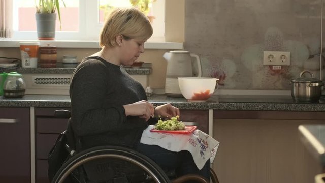 Woman in wheelchair cutting vegetables for salad on her kitchen