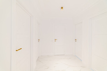 White empty corridor with white doors and gold fittings and ceiling lights. Home design