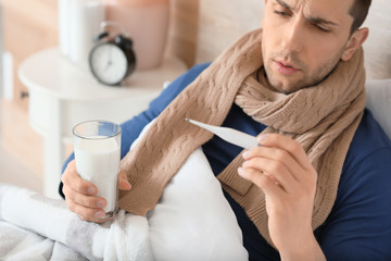 Young man ill with flu drinking milk in bed