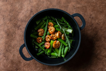 roasted shrimps in green esparagus in a black pan