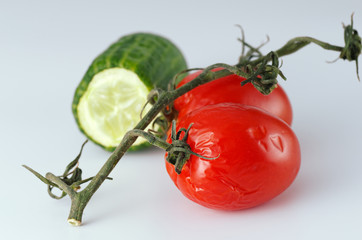 Wrinkled tomatoes and a half of cucumber lie on a table. Light gray background. Soft shadows. Selective focus.