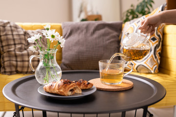 Hand of young female with teapot pouring green herbal tea into cup