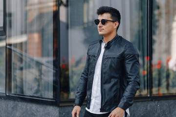young stylish guy in glasses in black leather jacket on glass background