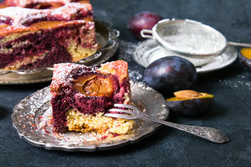 Tasty plum cake with pieces of fruit and powdered sugar on a dark background
