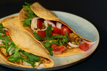 Plate with Mexican cuisine, large tacos with vegetables and meat on black background.