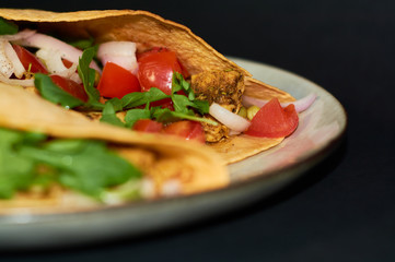 Plate with Mexican cuisine, large tacos with vegetables and meat on black background.