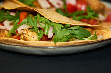 Plate with Mexican cuisine, large tacos with vegetables and meat on black background.
