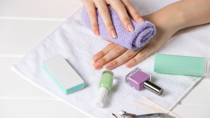 Obraz na płótnie Canvas Manicure. The woman wipes her hand with a towel. Manicure tools, nail polishes. Home nail care, SPA, beauty. Long natural nails. Beauty salon.