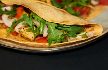Plate with Mexican cuisine, large tacos with vegetables and meat on black background.