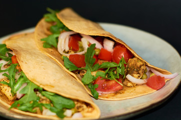 Plate with Mexican cuisine, large tacos with vegetables and meat on black background.