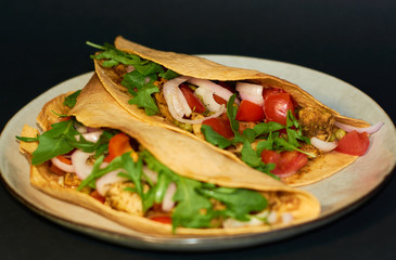 Plate with Mexican cuisine, large tacos with vegetables and meat on black background.