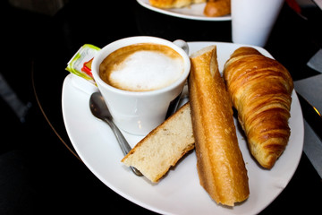 Parisian classic Breakfast. On a white plate, a baguette, a croissant, a Cup of coffee with foam, a spoon and jam in a package. France.