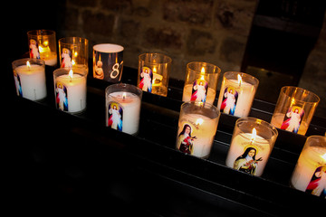 Candles in the Catholic Church in honor of the commemoration. They depict saints. A warm,...