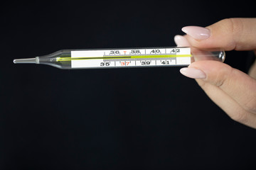 Female holds mercury medical thermometer in hand which shows above 37 degrees isolated on black background. Body temperature checking, healthcare, disease symptoms