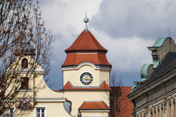 Fototapeta na wymiar Turm eines klassischen Gebäudes mit gelber Fassade, rotem Dach aus Ziegeln und einer Uhr am Turm. Bewölkter Himmel. Architektur in Bayreuth, Deutschland. 