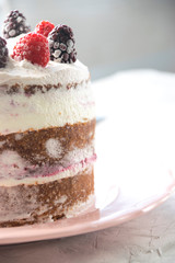 Side view of a sponge cake filled with whipped cream and berries sauce topped with raspberries and blackberries as a decoration. Naked cake concept