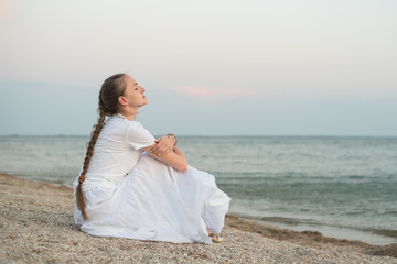 Fototapeta na wymiar Young beautiful woman with long braid sits by the sea and dreams