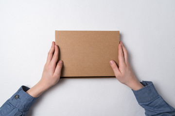 Cardboard box in children's hands on white background. Top view. Copy space.