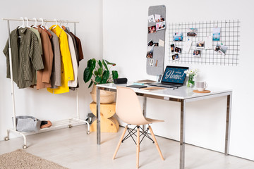 Workplace of contemporary fashion designer with supplies on desk and rack