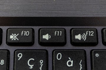 A close up portrait of the mute, volume up and volume down buttons on a laptop keyboard. The physical keys are black with a white icon on them to display what the button does.