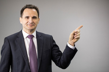 handsome 40s businessman smiling pointing at copy space with his forefinger isolated on grey background. business bank offer, sale, insurance, investment, technology, high quality
