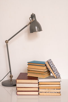 Lamp over stacks of books and manuals on table or workplace of student