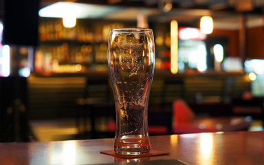 Evening. Empty beer glass on the table in a dark bar, panoramic view. Foam stains inside the glass