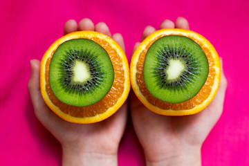 kiwi with orange and children`s hands on a pink background