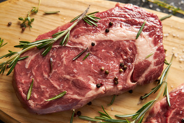 Raw fresh rib-eye steak with spices lies on a wooden board.