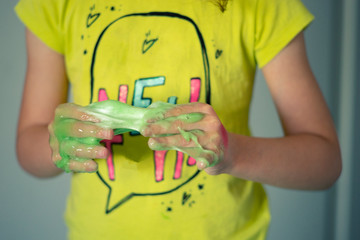 Young girl getting her hands stuck with a sticky green slime.