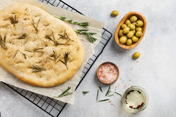 Italian traditional focaccia bread baking with aromatic seasonings and rosemary on a light gray background. Top view.