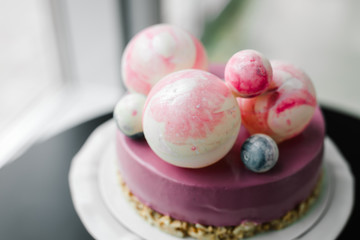 purple cake with pink and blue chocolate balls on a white stand