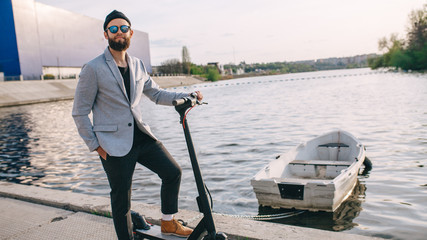 Young hipster man in a suit riding an electric scooter in bright sunny day. Ecological transportation concept.