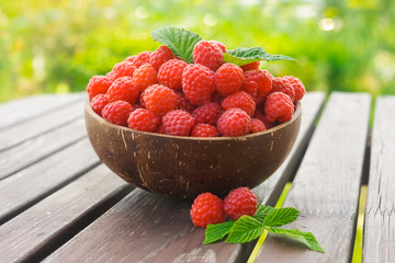 Bowl with ripe raspberries on rustic wooden table with green background