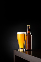 Glass of cold beer and a beer bottle on bar counter