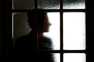 A photograph of a persons profile taken through a blurry door glass